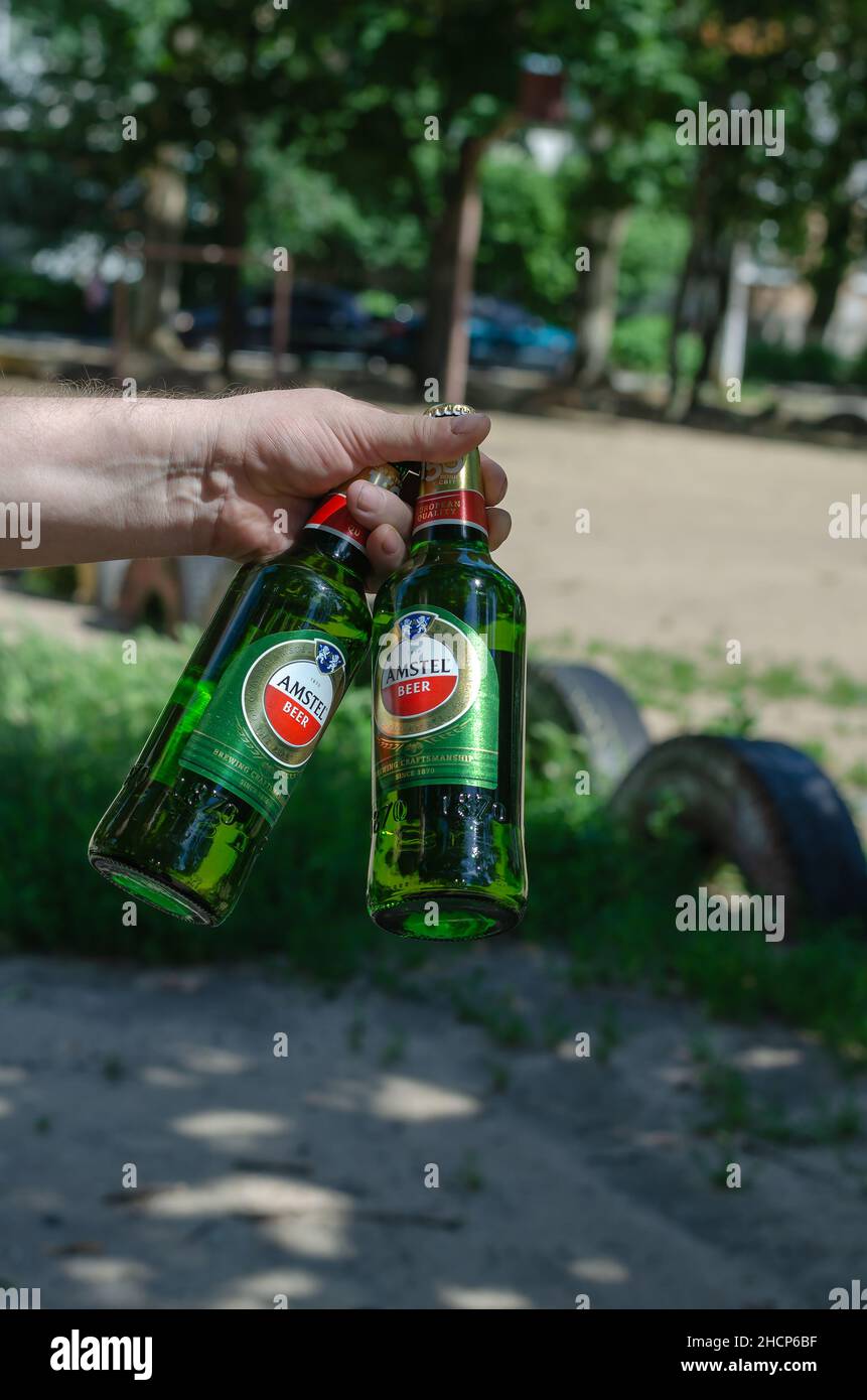 The hand holds two bottles of Amstel beer. Adult male with green bottles of alcoholic beverage. Nikolaev, Ukraine - 07 13 2021 Stock Photo