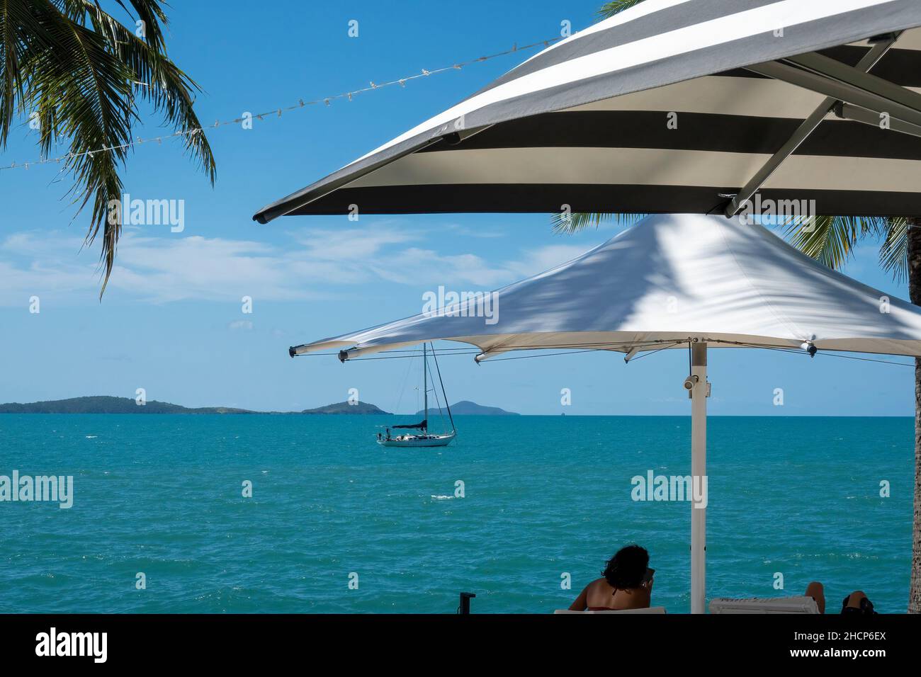 Tourists Relaxing Under Umbrellas Looking Out To See At A Yacht Sailing