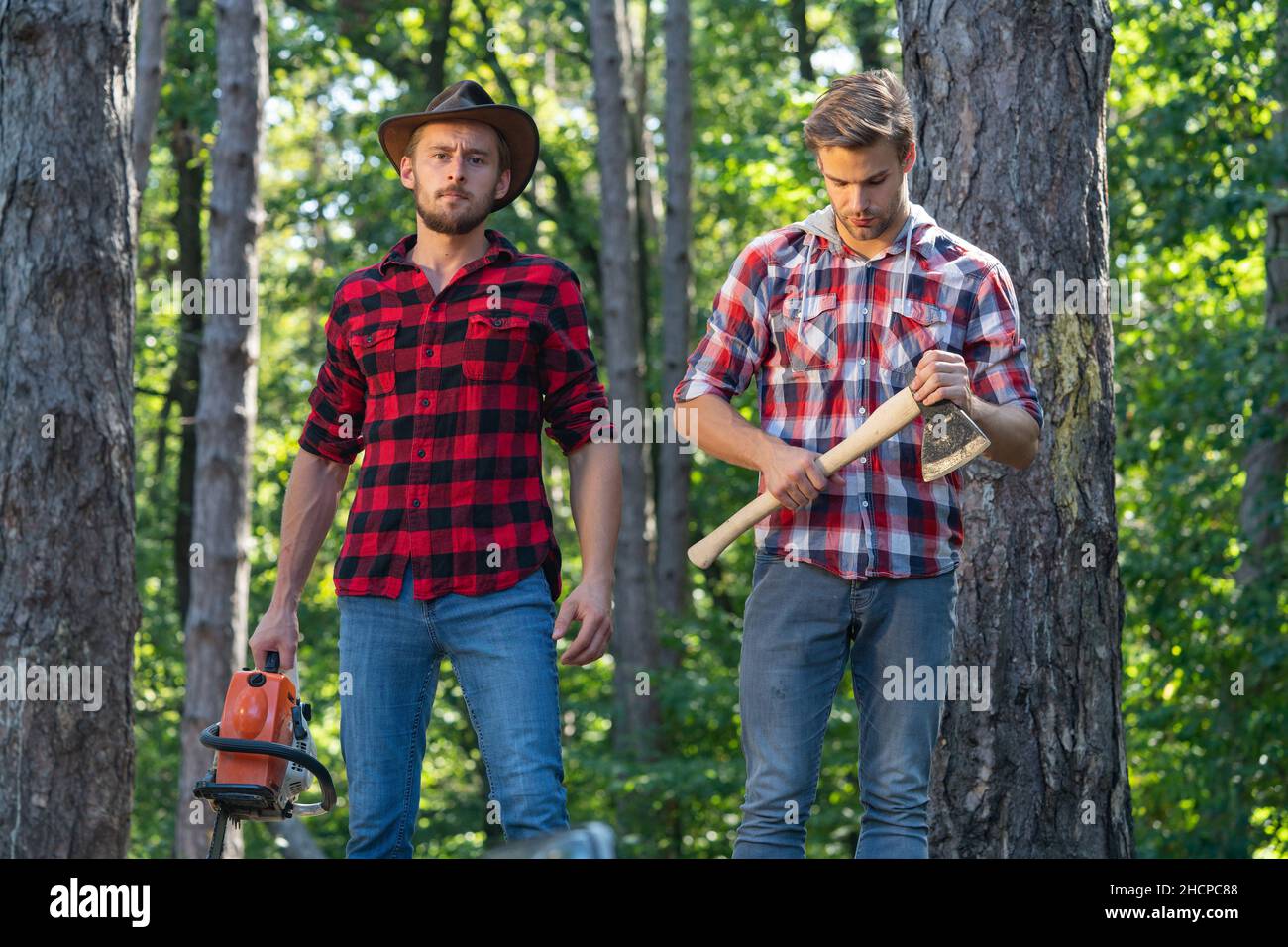 Two lumberjacks with chainsaw and axe. Male lumberjack in the forest