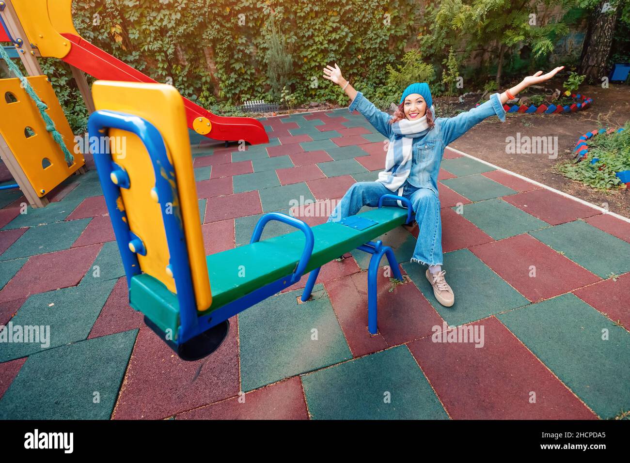 Infantile and childish happy woman or a teenage girl swings on seesaw. Concept of psychology and sociology of the new generation and growing up. Stock Photo