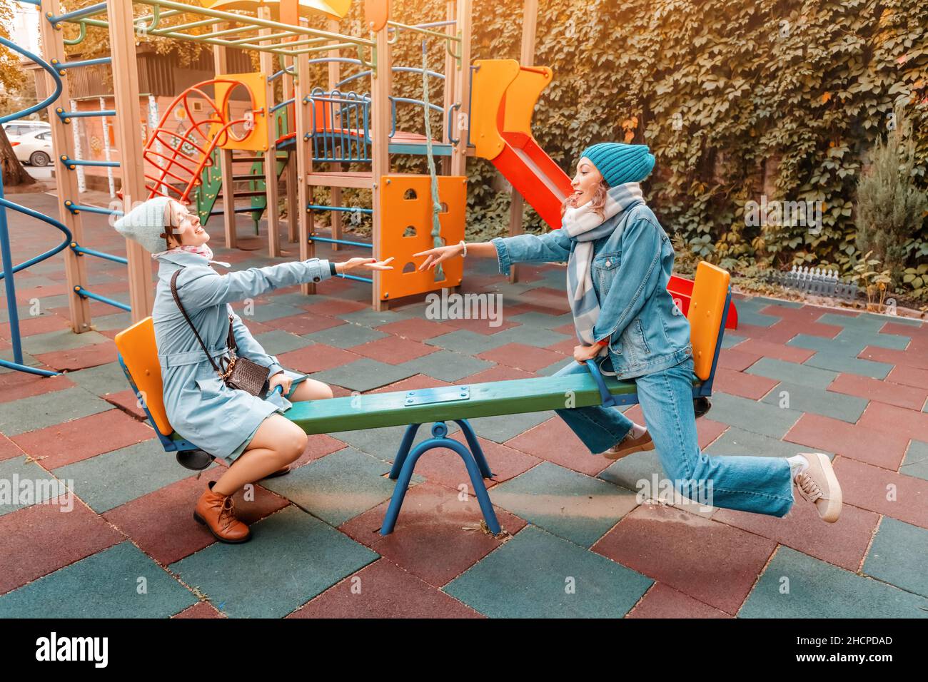 Two childish happy woman friends or teenage girl having fun on seesaw on a playground. Concept of psychology of the new generation and relations Stock Photo