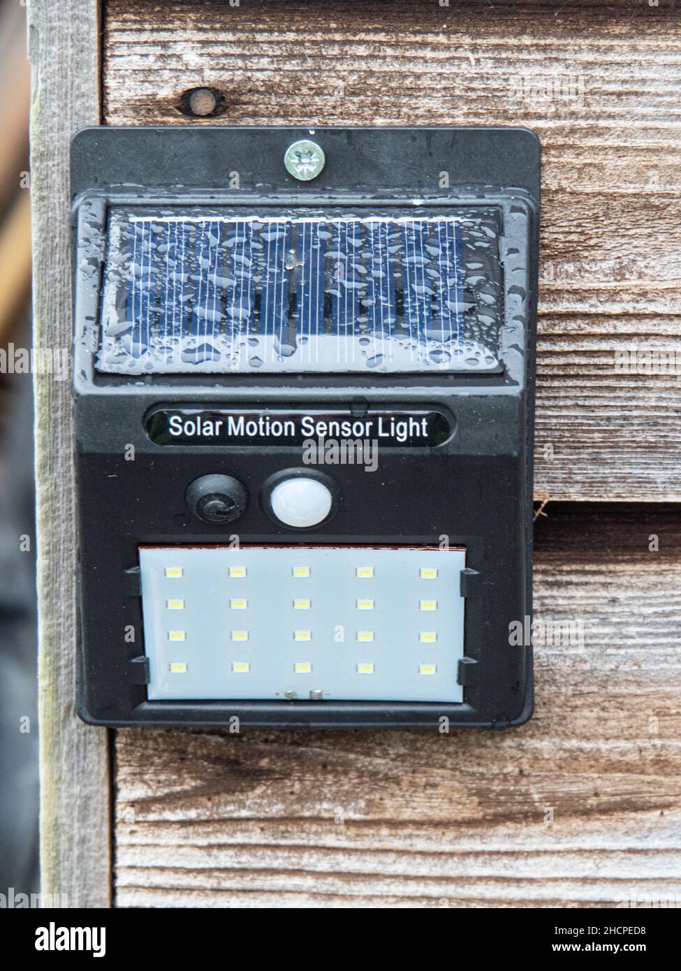 A solar powered motion sensor light with a LED array fixed to a wooden building.l Stock Photo