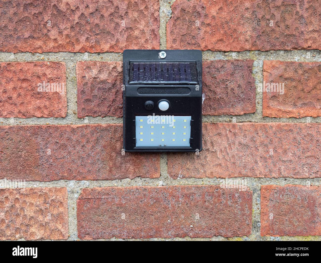 A solar powered motion sensor light with a LED array fixed to a brick wall Stock Photo