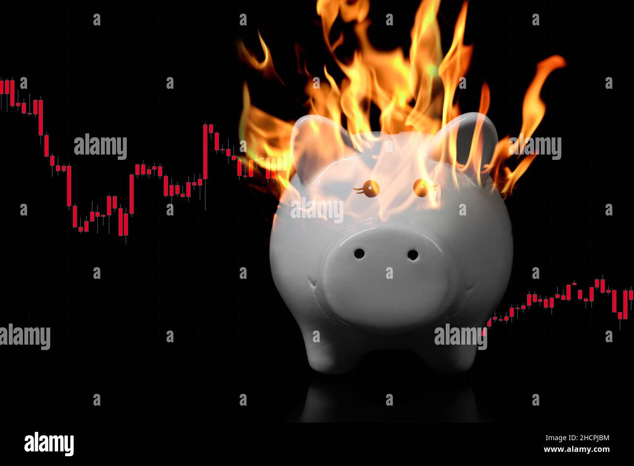 White piggy bank on fire on a very dark surface with descending red candle chart behind. Concept for economic crisis, inflation, devaluation Stock Photo
