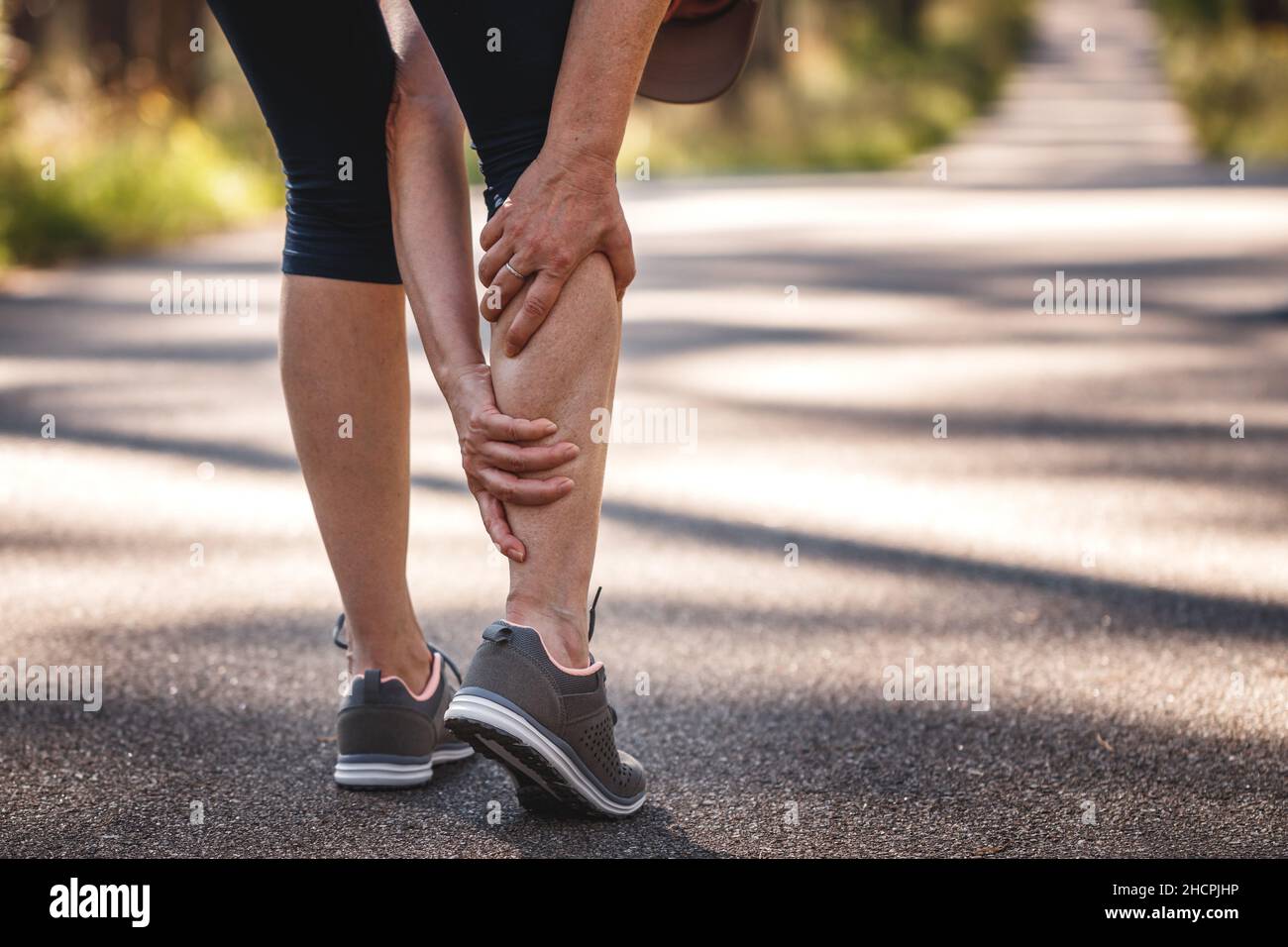 Woman feeling pain of her legs during jogging. Calf muscle cramp. Underestimating the warm-up exercise before running Stock Photo