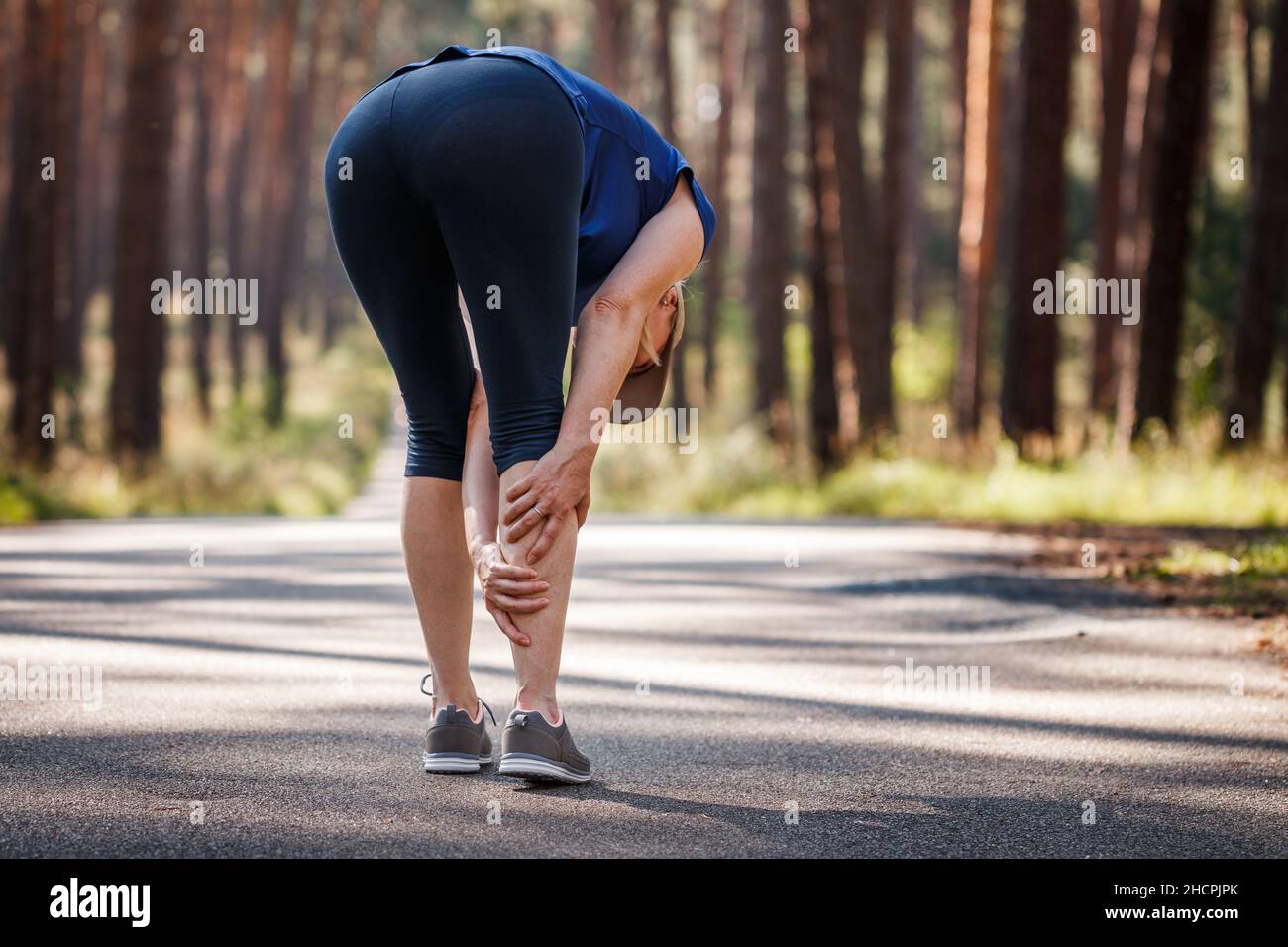 Calf muscle cramp. Woman feeling pain of her legs during jogging. Underestimating the warm-up exercise before running Stock Photo
