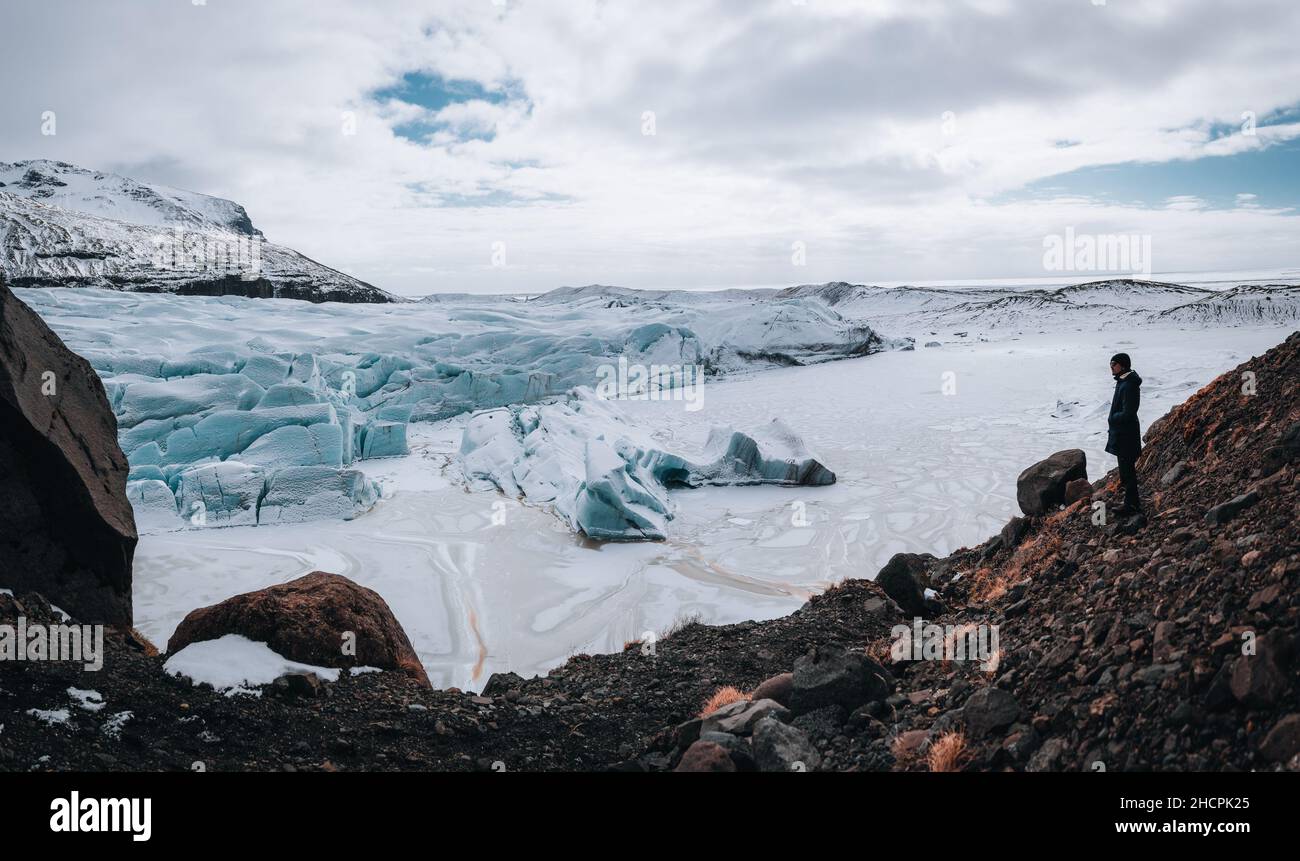 A man standing in front of a massive blue glacier at Solheimajokull and Vatnajokull and Svinasfellsjokull glacier in South Iceland on a sunny winter Stock Photo