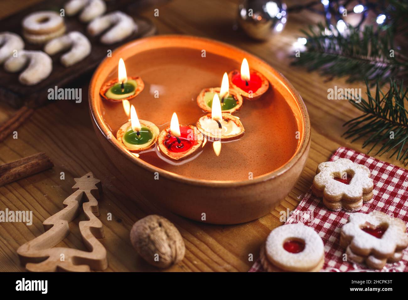 Christmas tradition. Candles made from nut shell floating on water. Decoration and christmas sweets on table Stock Photo