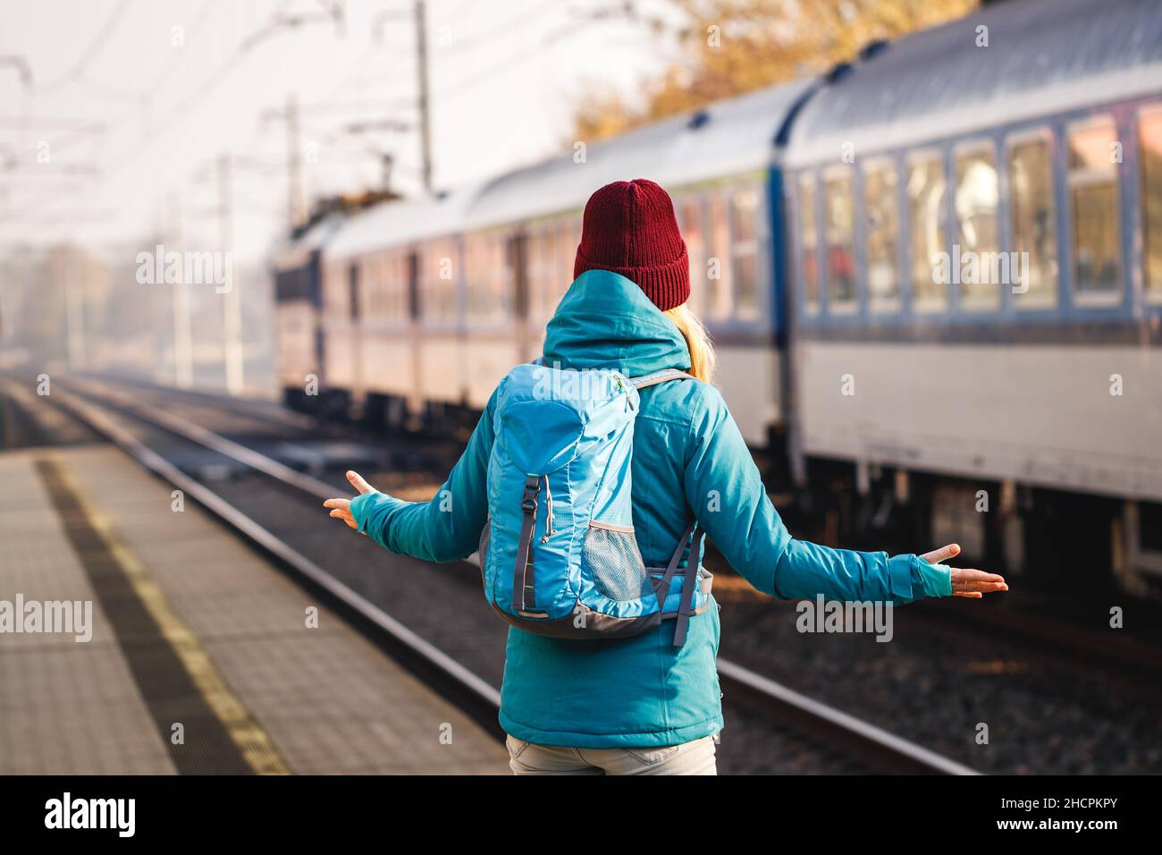 Confused tourist standing at wrong railway station platform. Disappointment during traveling. Woman with backpack looking at leaving train. Traveler Stock Photo