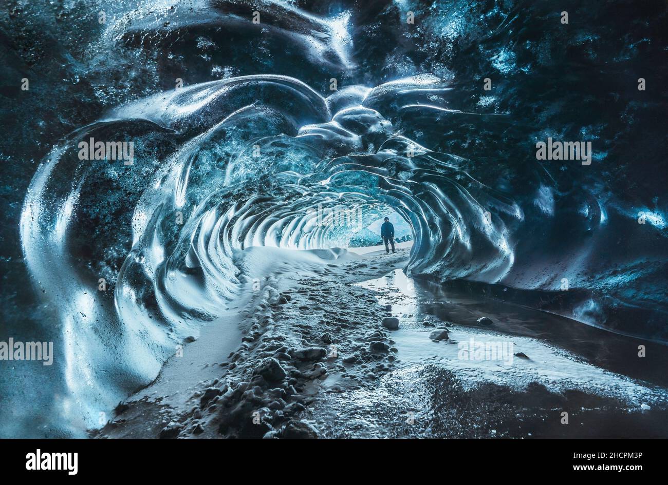 Blue crystal ice cave entrance with tourist climber and an underground river beneath the glacier located in the Highlands in Iceland Stock Photo