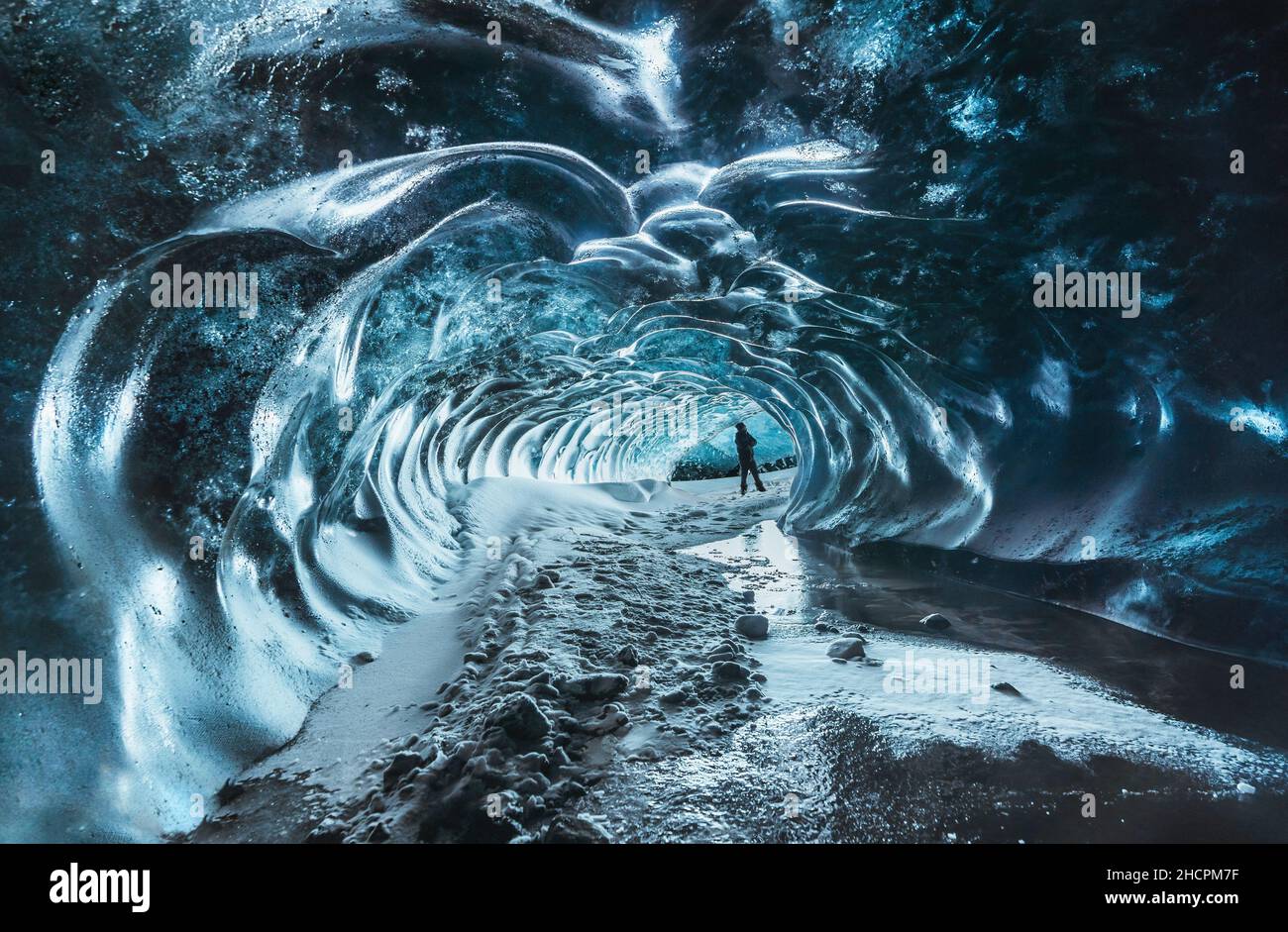 Blue crystal ice cave entrance with tourist climber and an underground river beneath the glacier located in the Highlands in Iceland Stock Photo