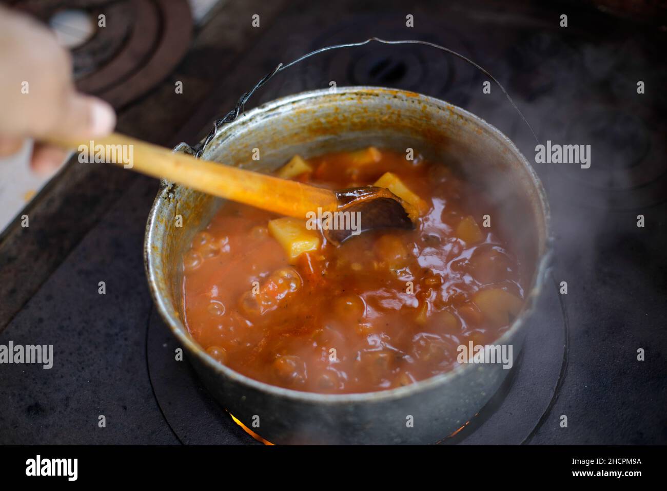 Cast iron cauldron boiling a goulash stew over a wood burning stove made from red bricks in the backyard of a rural house in Romania. Stock Photo