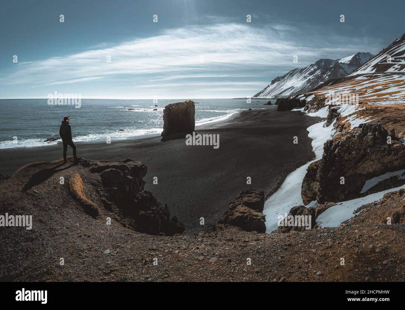 Person standing at black sand beach in Iceland. Fauskasandur near village of Djupivogur. Black sand beachwith snow and beautiful sunny weather Stock Photo