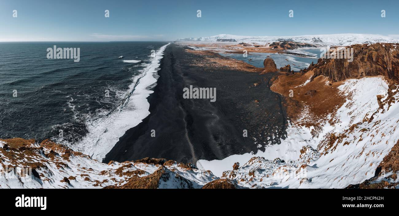 View from Dyrholaey lighthouse in Iceland looking out over the black sand beach below during winter with snow and beautiful sunny weather. Stock Photo