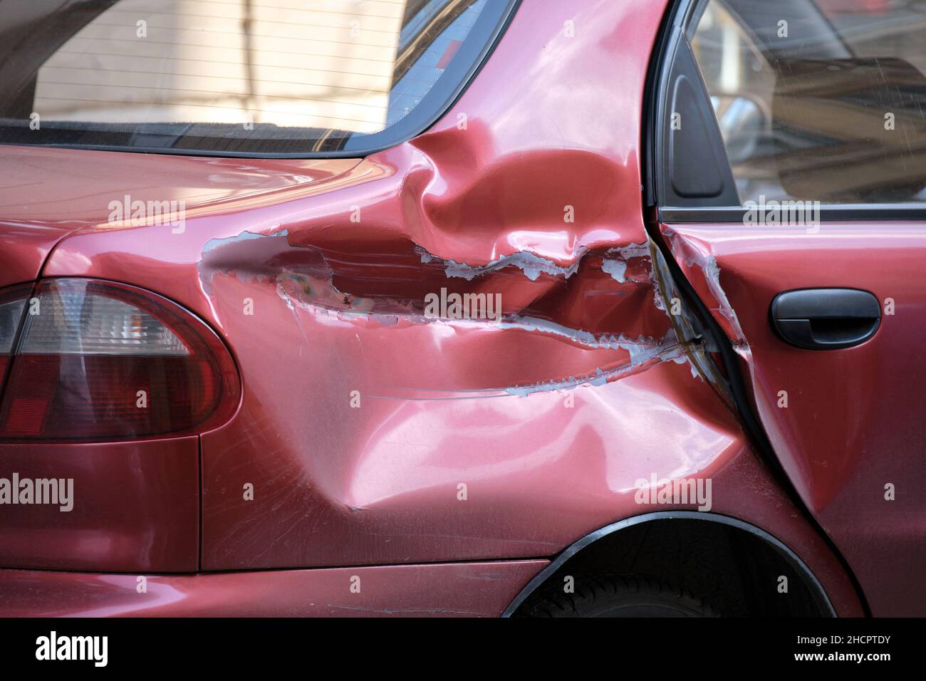 Dented car with damaged body parked on city street side. Road safety