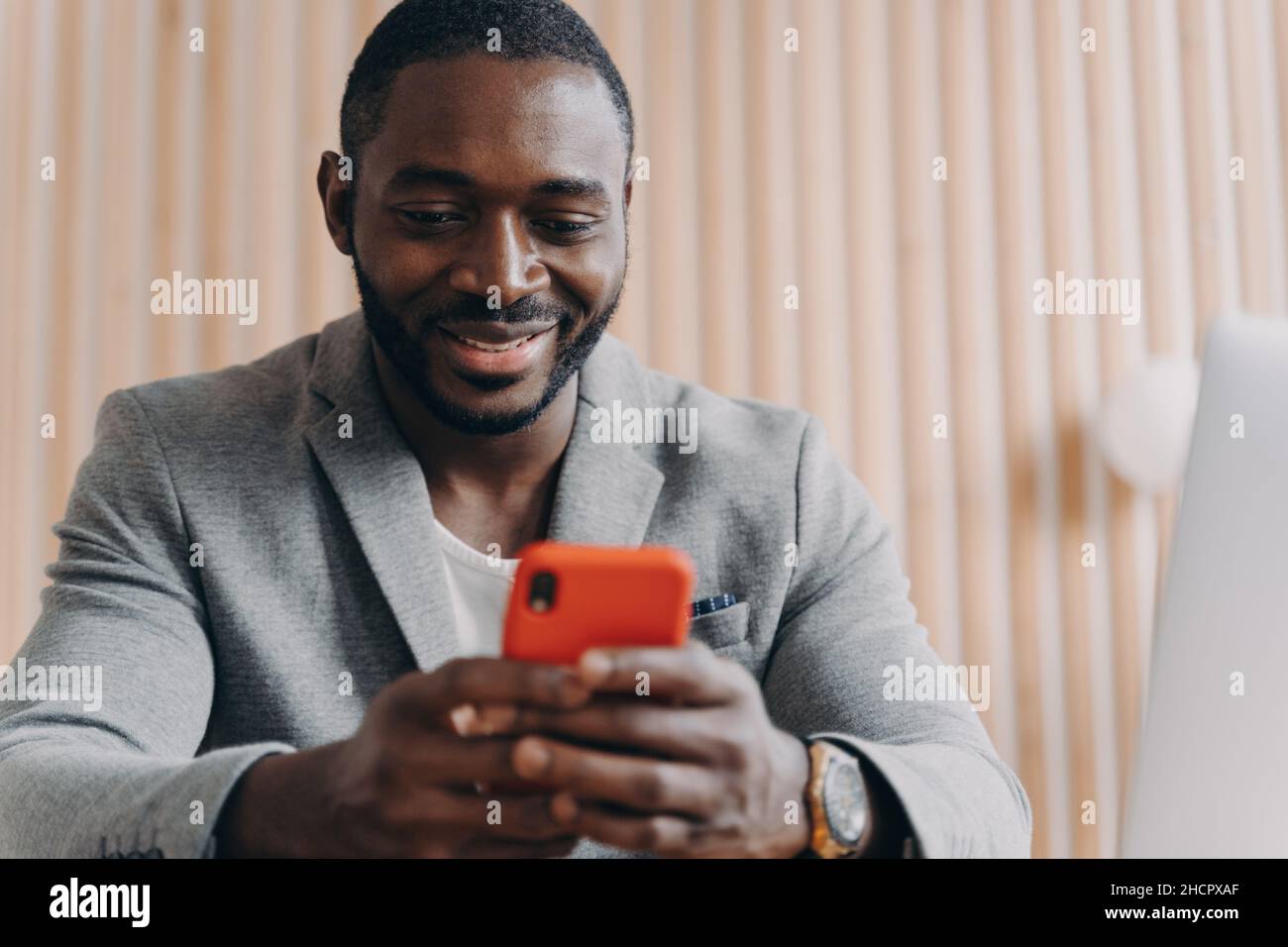 Cheerful young afro american man chatting online on smartphone looking on phone screen with smile Stock Photo