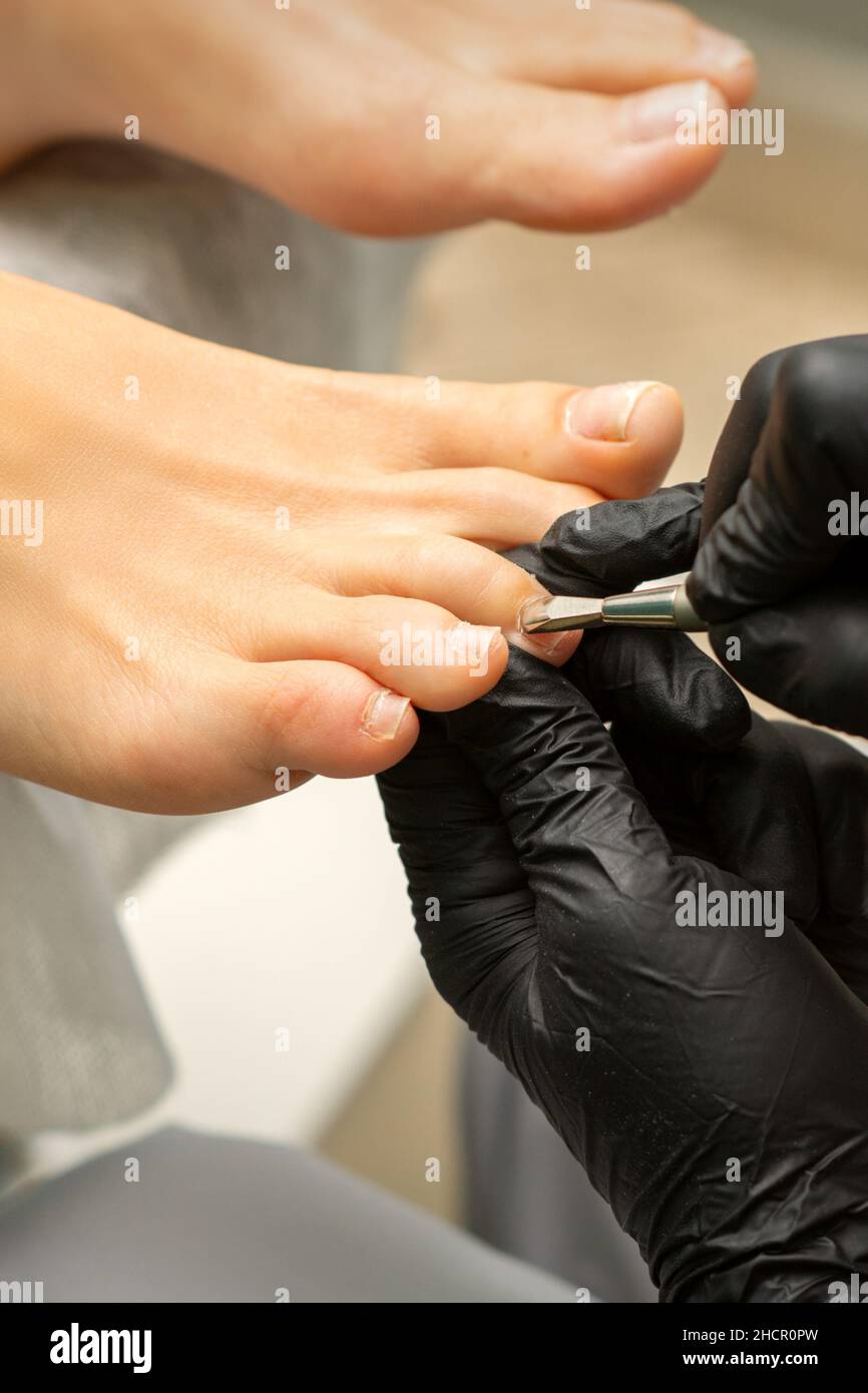 Cuticle Removal on Toes. Hands in black gloves of pedicure master