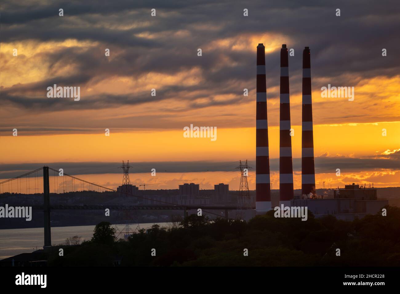 Power plant smoke stacks silhouetted against a dramatic sunset. Stock Photo