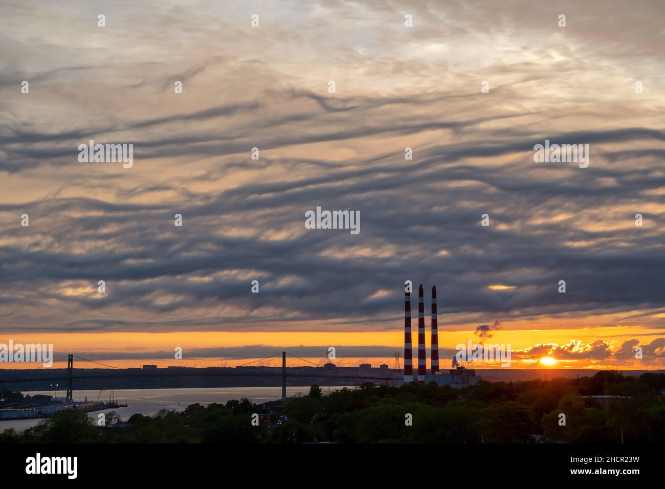 Power plant smoke stacks silhouetted against a dramatic sunset. Stock Photo