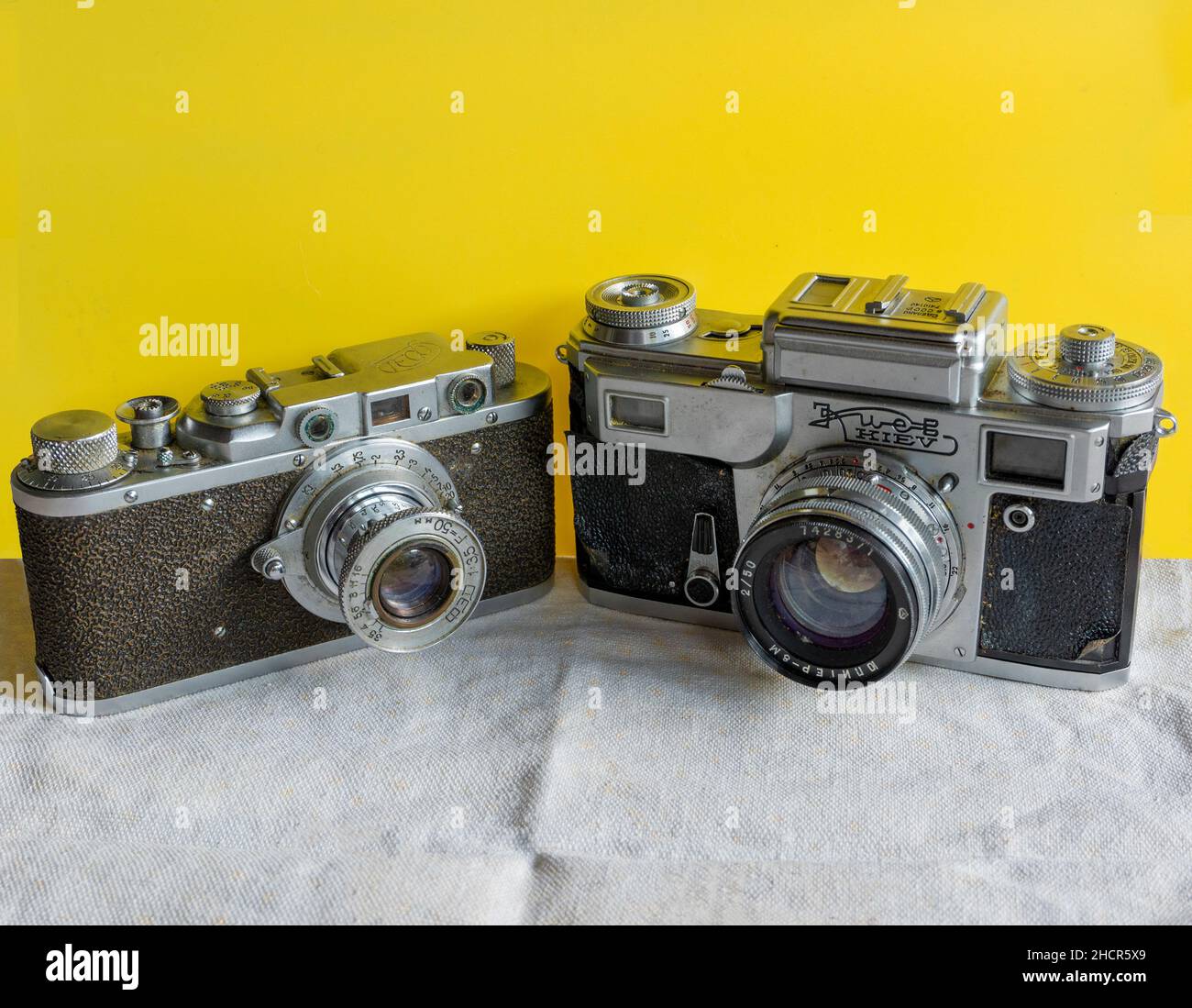 An old war correspondent's cameras lies on a tablecloth against a yellow background Stock Photo