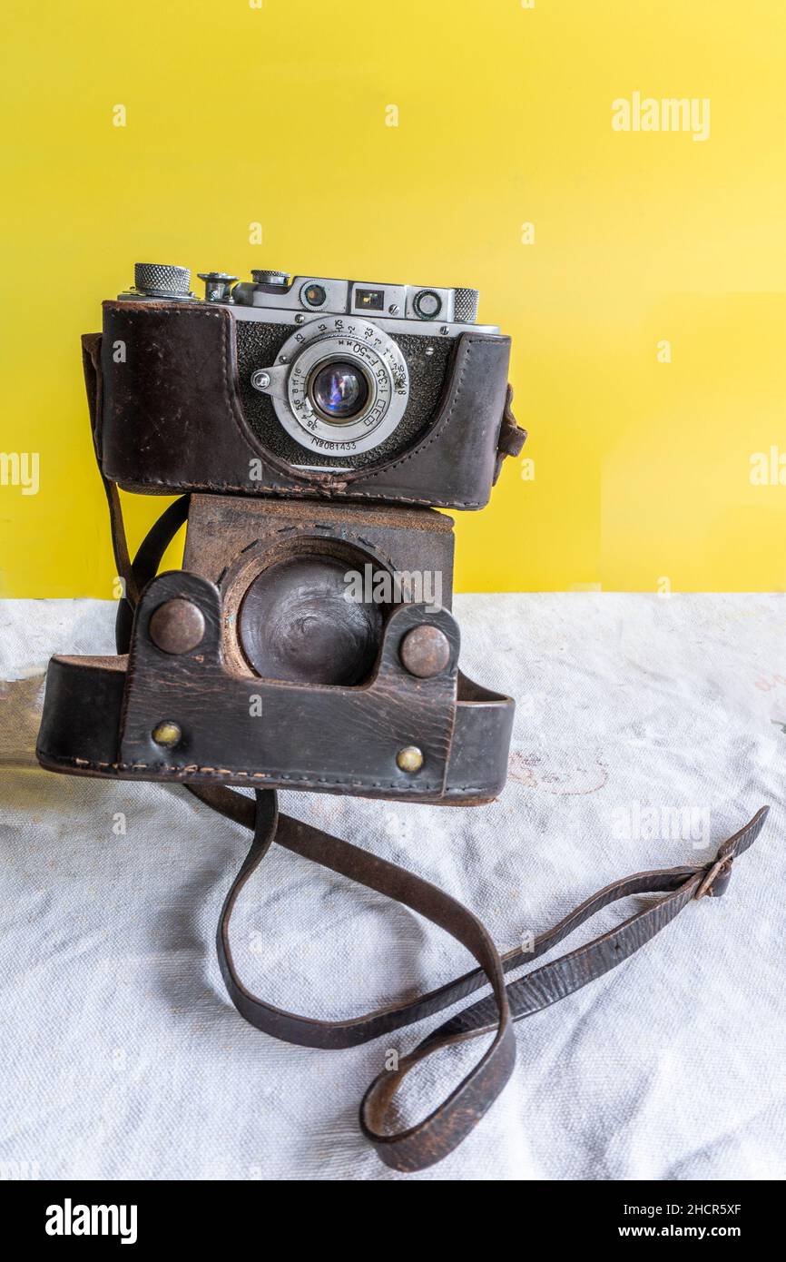 An old war correspondent's camera lies on a tablecloth against a yellow background Stock Photo