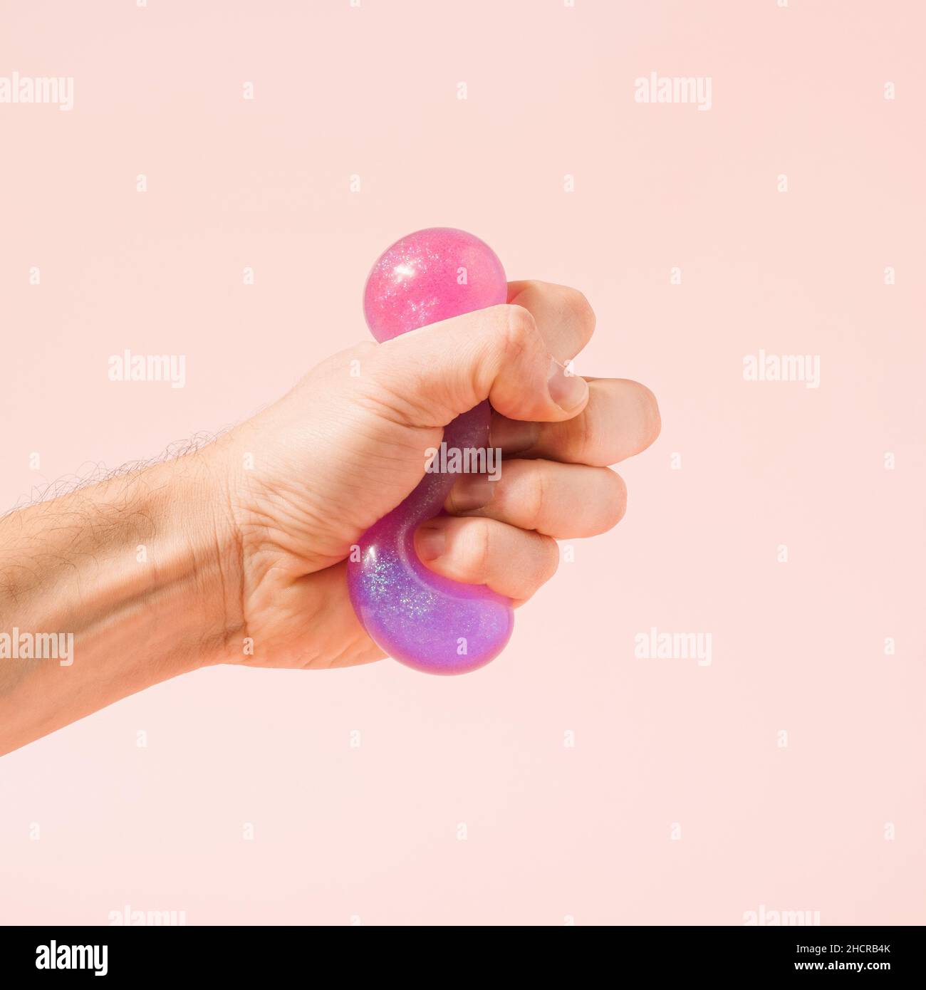 Hand squeezing violet purple glitter slime on a pastel pink background. Immersive reality conceptual background. Stock Photo