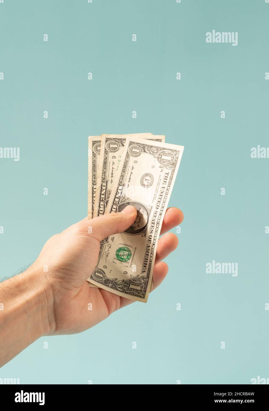 Hand holding one dollar bills on a pastel blue background. US economy conceptual background. Stock Photo