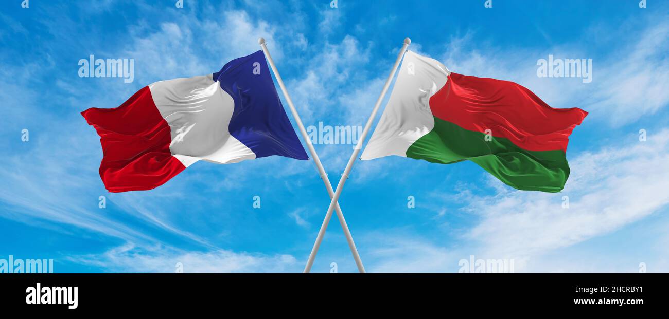 crossed national flags of France and Madagascar flag waving in the wind at cloudy sky
