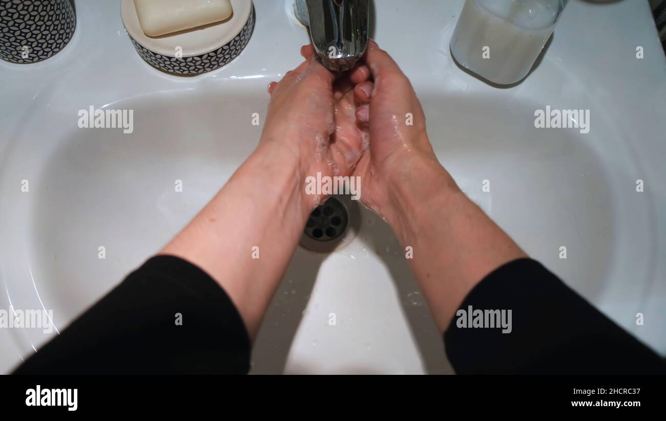 Woman washing hands with soap in bathroom. Close up of female hands ...