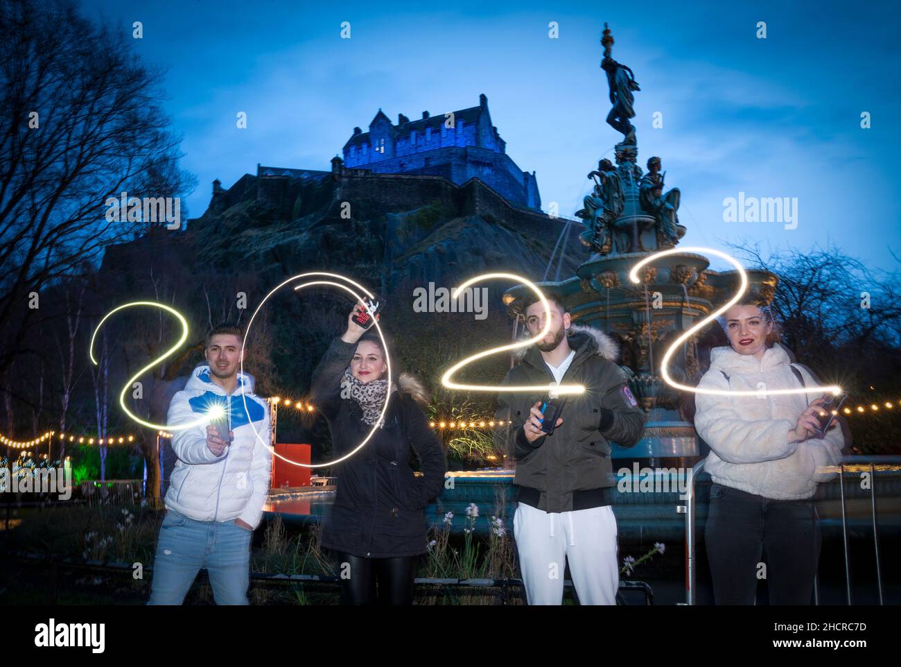 (left to right) Alex Badea, Maria Mutuliga, Livia Miheala and Alex Rudolff, from Dorset, use their smartphones to spell out 2022 in Edinburgh's Princes Street Gardens during New Year's Eve. Picture date: Friday December 31, 2021. Stock Photo
