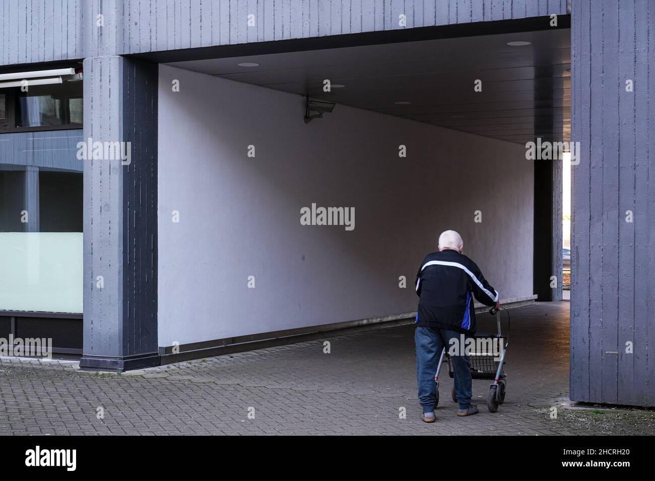 A white-haired man walks with his walker from a backyard into a passageway to the street. Stock Photo
