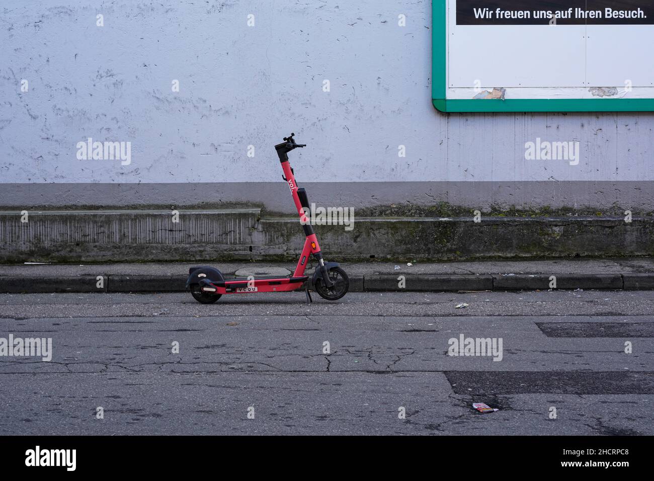 A red electric scooter parked by the roadside in front of a wall. Stock Photo