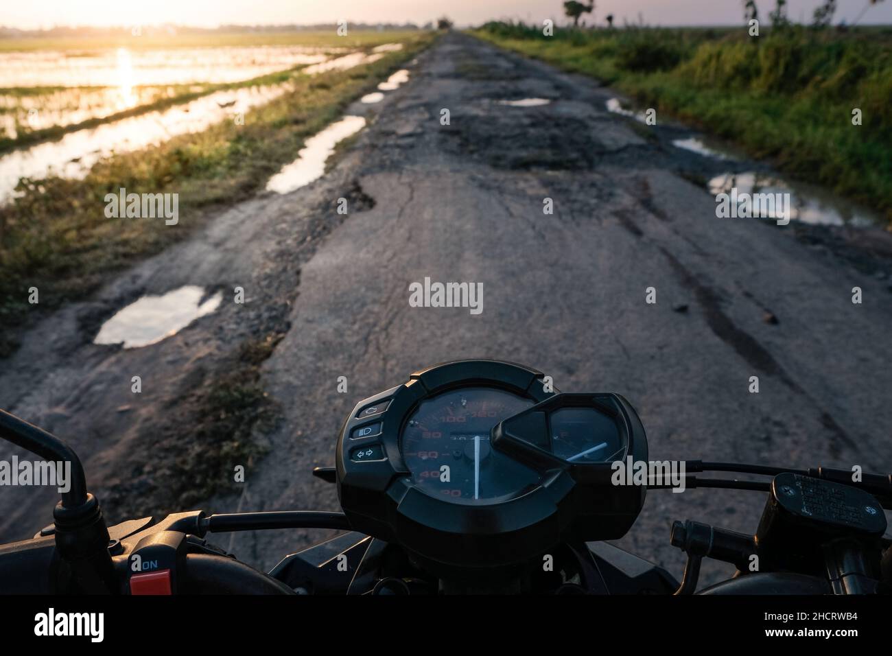 View of the damaged road with potholes with puddles from the top of the motorbike Stock Photo