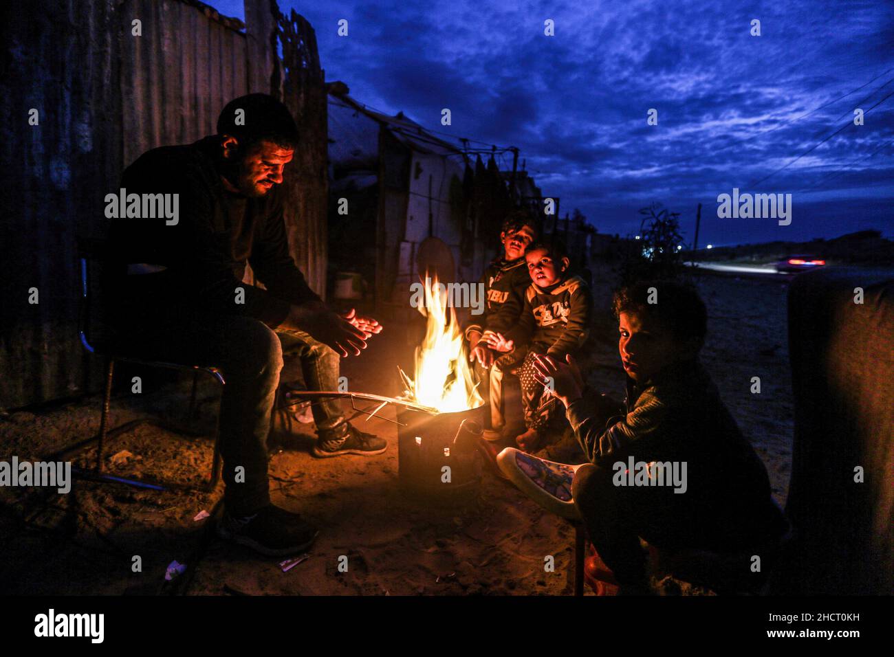 A Palestinian family sits around fire to warm up in front of their ...