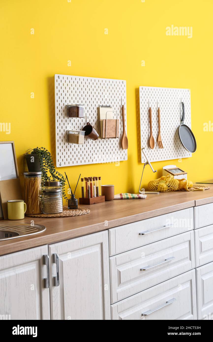 Peg boards with kitchenware hanging on yellow wall Stock Photo