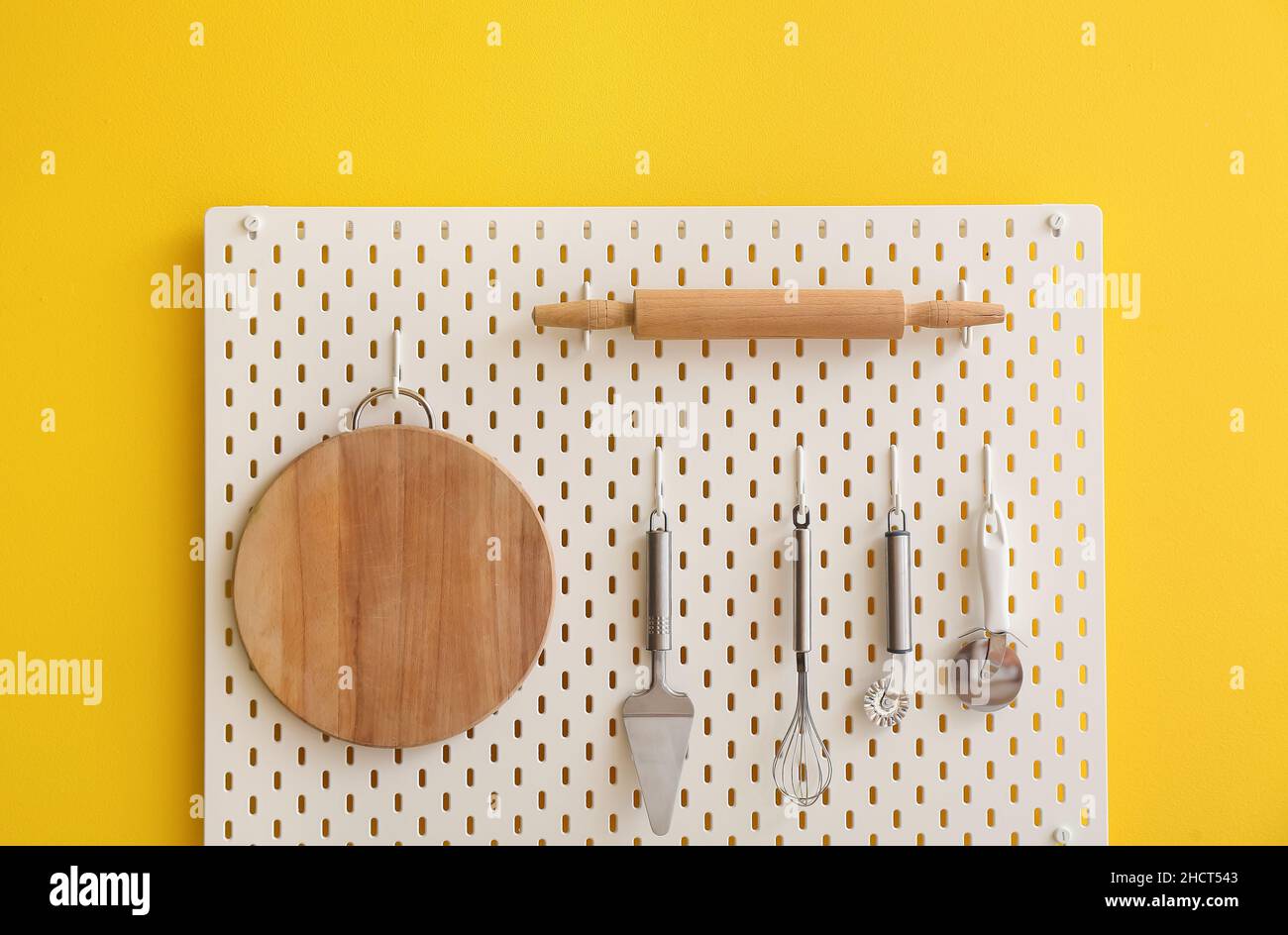 Peg board with kitchenware hanging on yellow wall Stock Photo