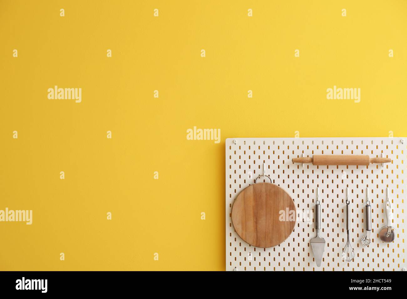 Peg board with kitchenware hanging on yellow wall Stock Photo