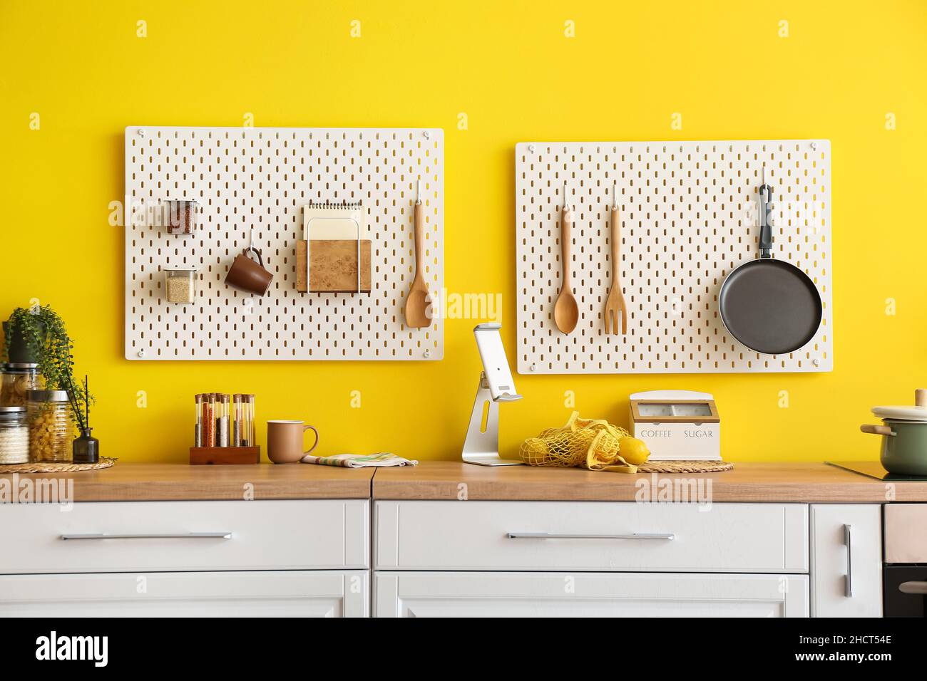 Peg boards with kitchenware hanging on yellow wall Stock Photo