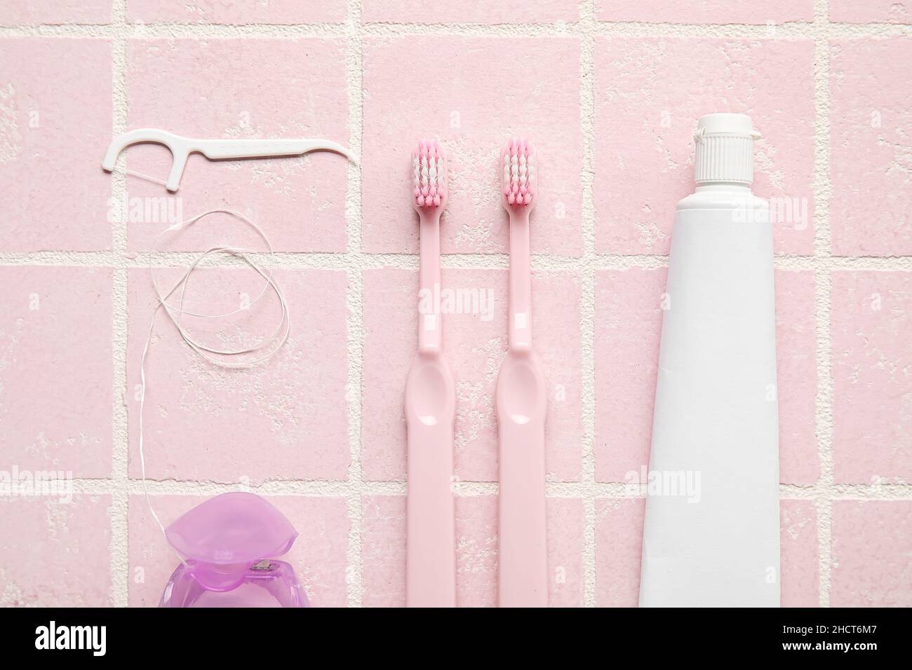 Dental floss with toothpicks, brushes and paste on pink tile background ...