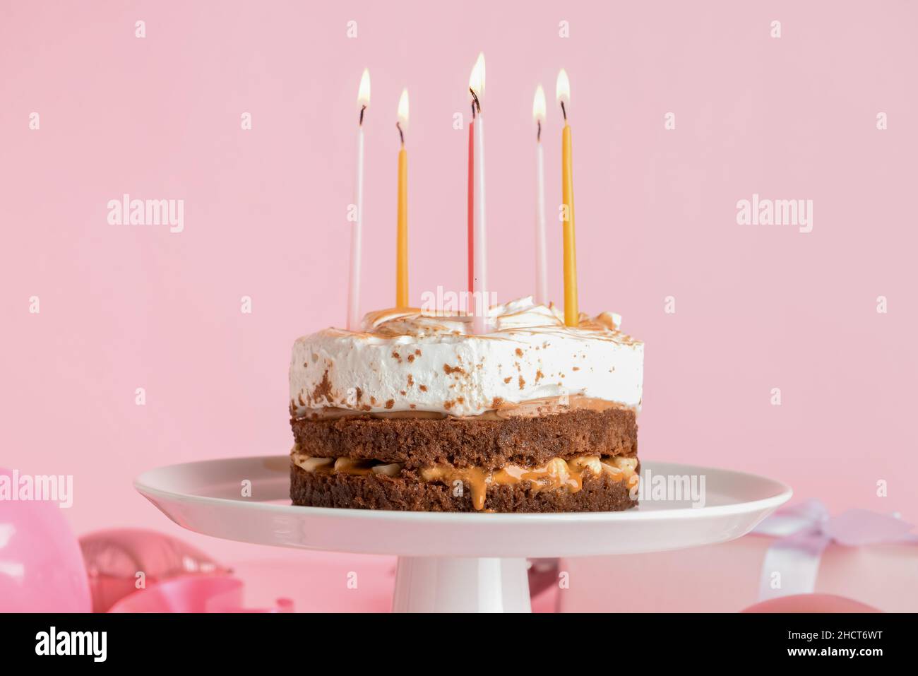 Stand with tasty birthday cake and burning candles on pink background ...