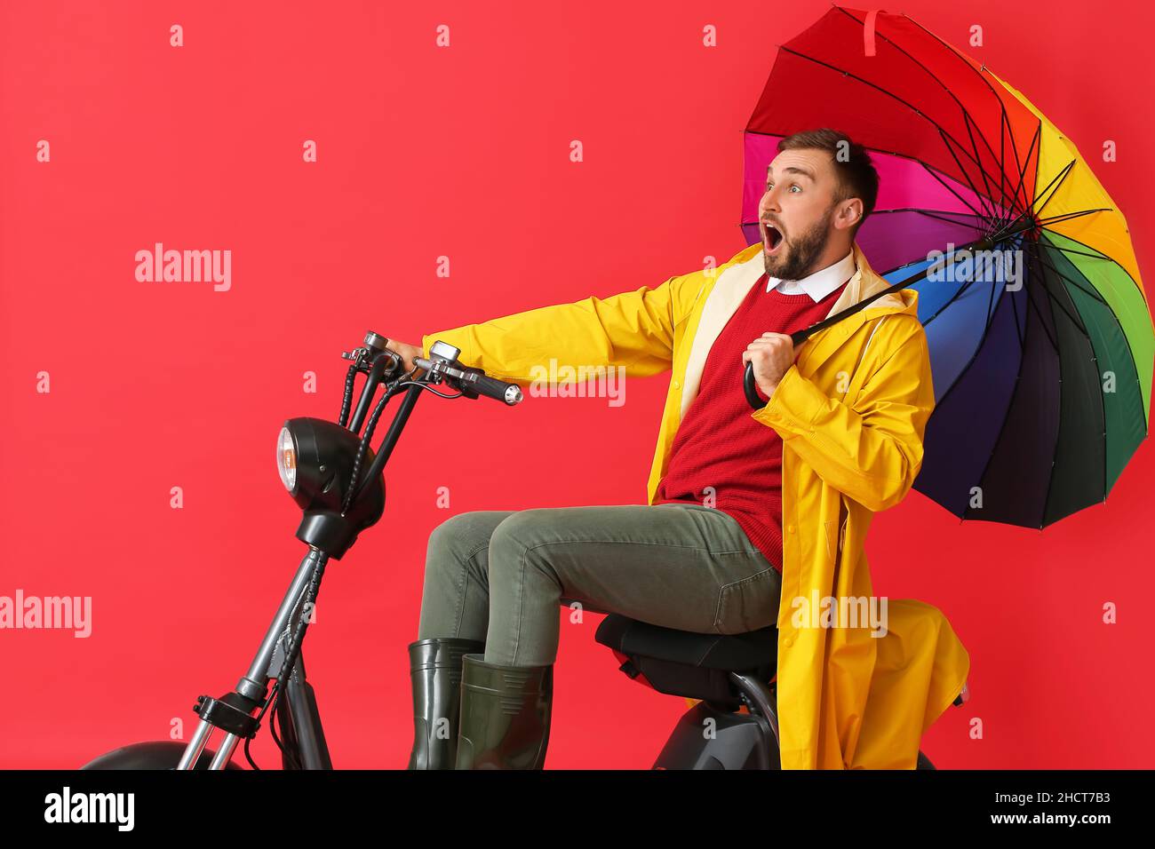 Surprised man in raincoat and with umbrella riding bike on color