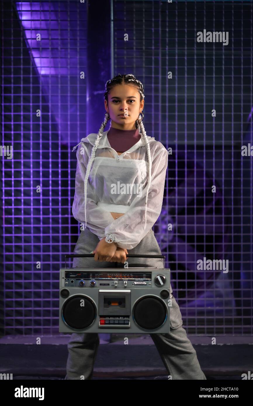 Young girl with white braids with a boombox on an urban background, purple lights, 80s style, retro photography, vertical photo Stock Photo