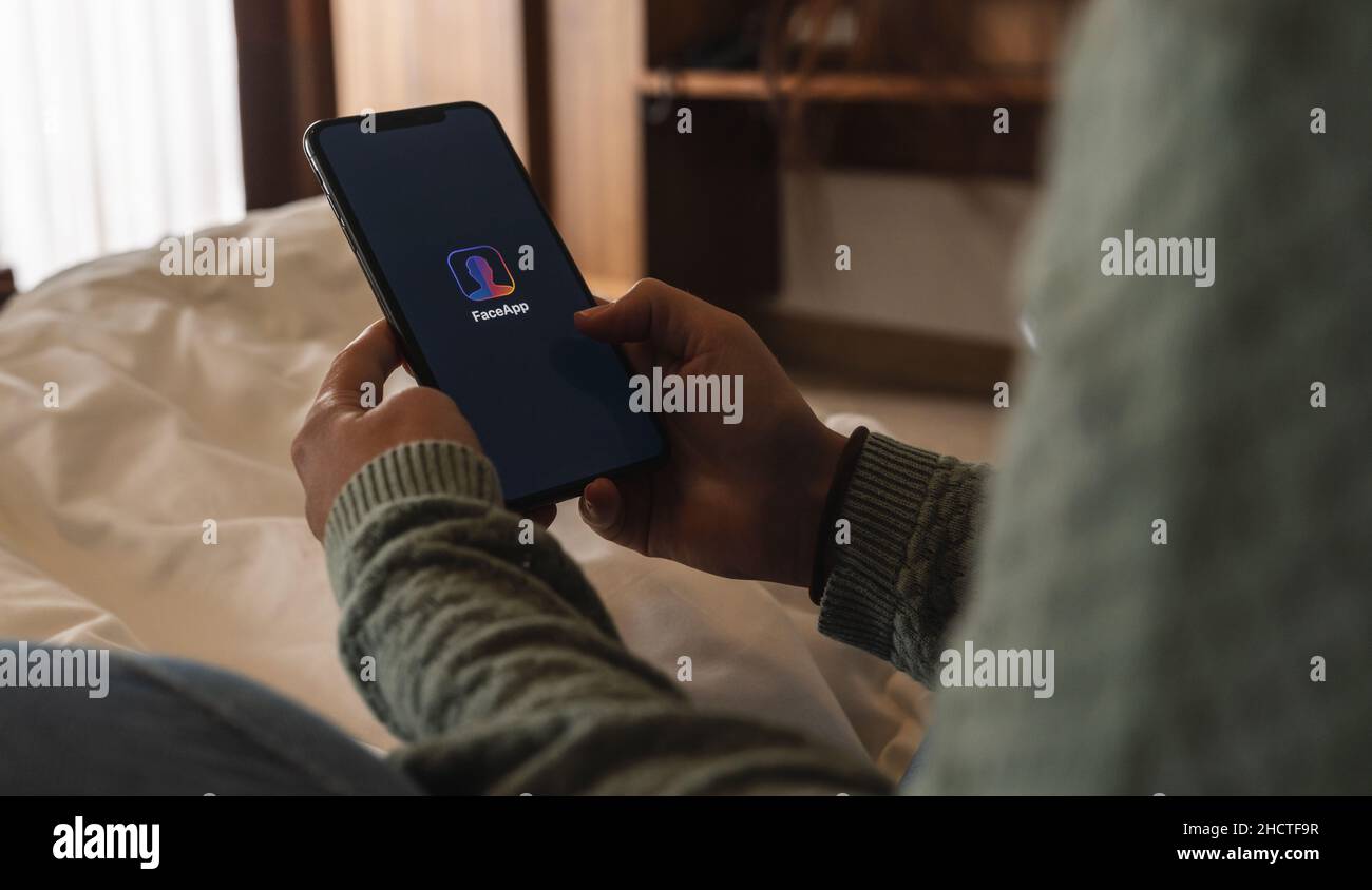 Woman holding a iPhone Xs opening Face app at bed, faceapp is a popular ...