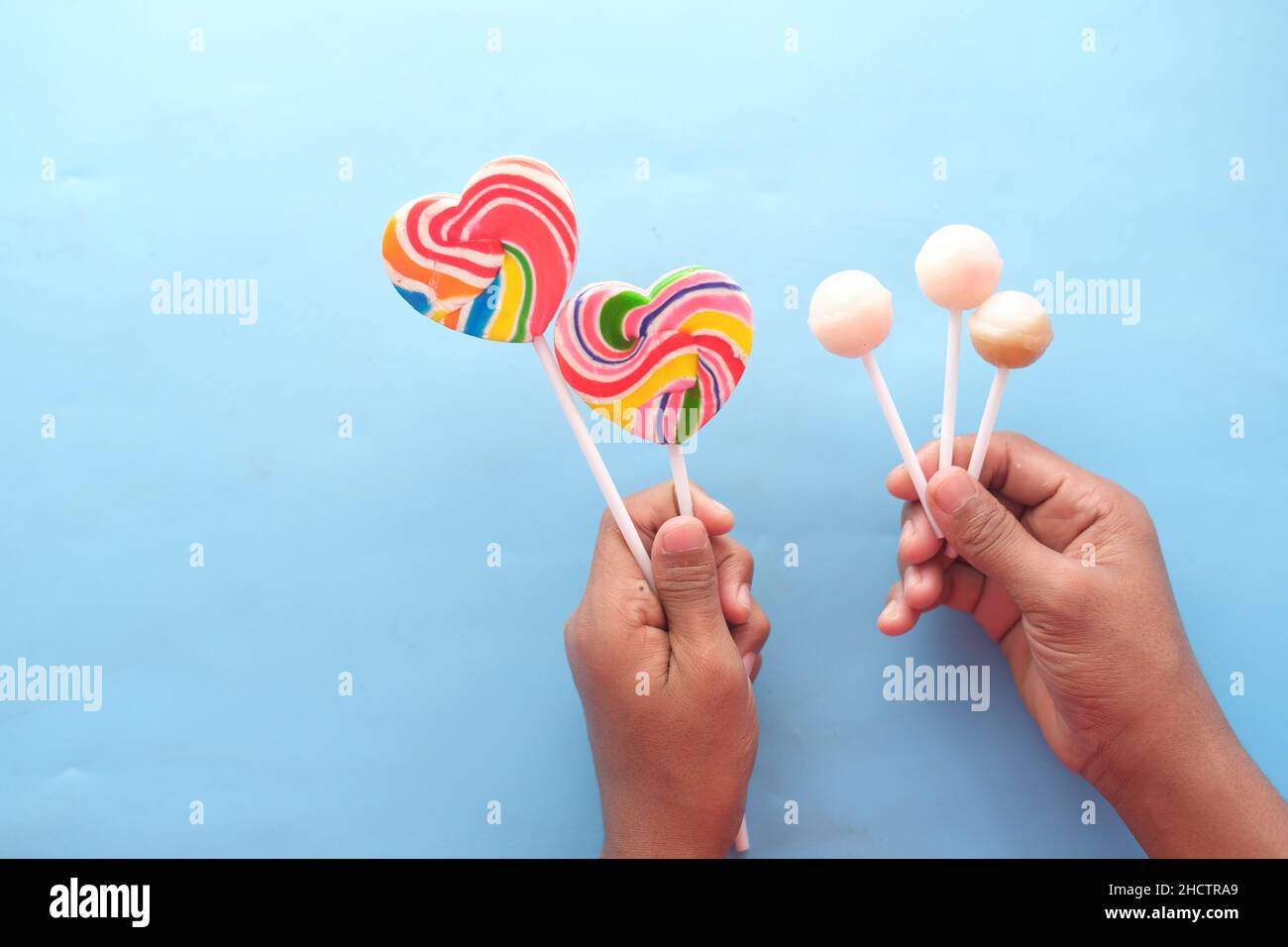 holding rainbow heart shape lollipop on blue background  Stock Photo