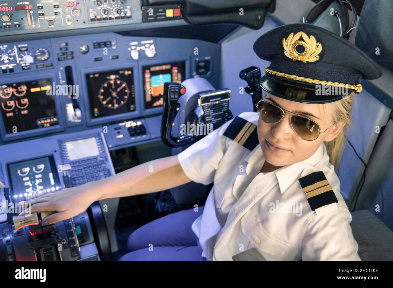 Beautiful blonde woman pilot wearing uniform and hat with golden wings - Modern aircraft cockpit ready for take off Stock Photo