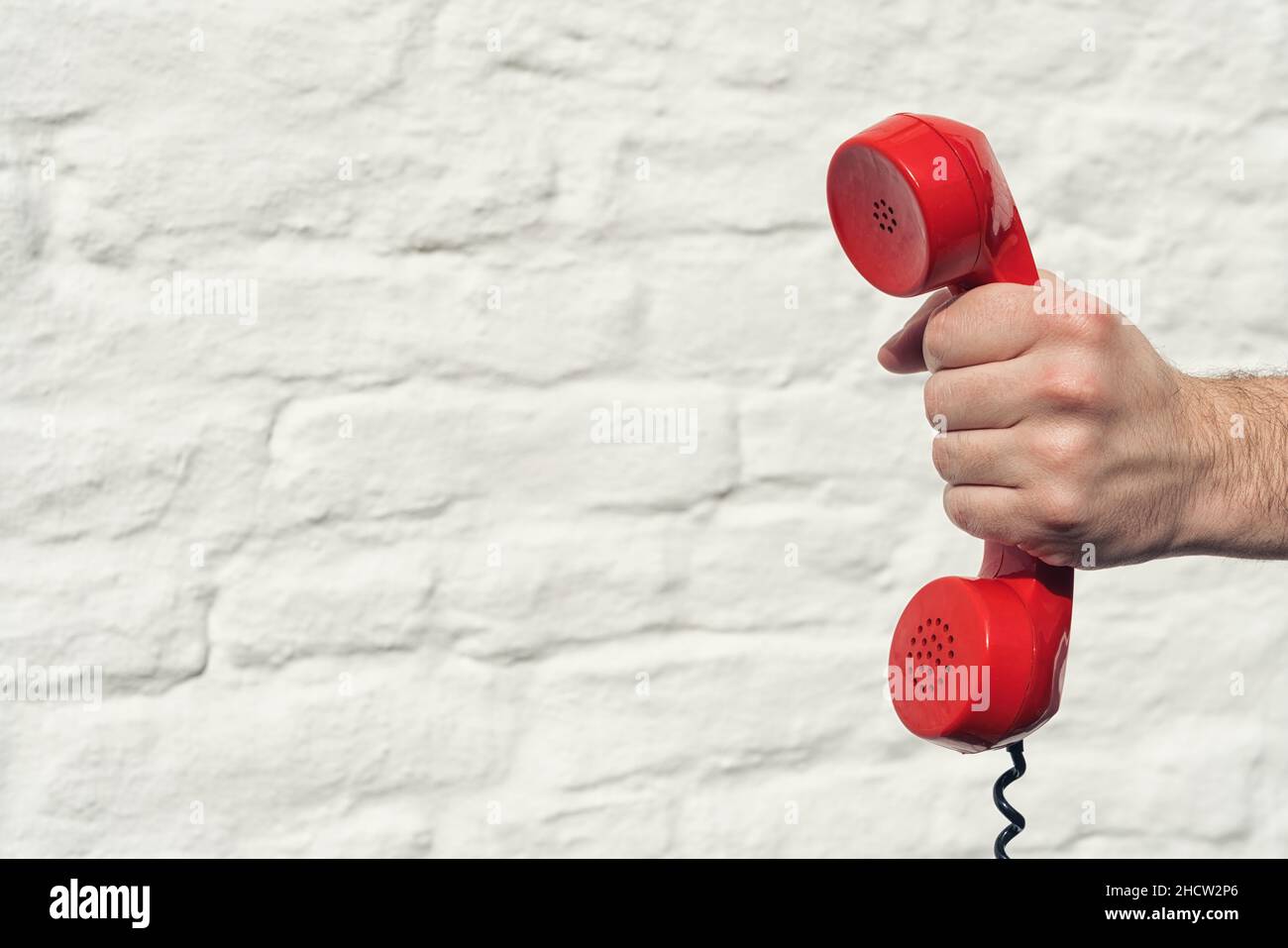 red handset in hand on a brick wall background Stock Photo