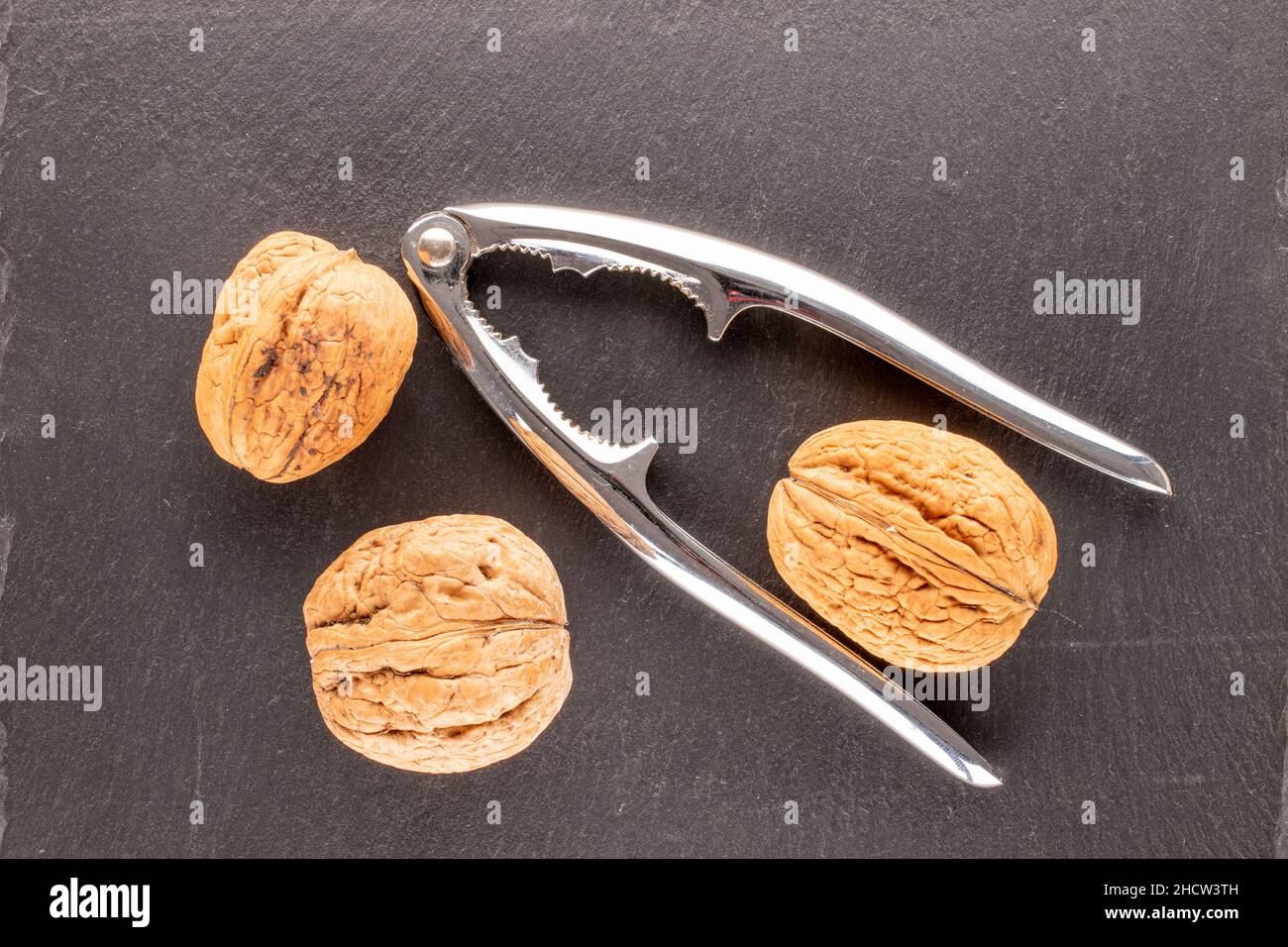 Three walnuts and a metal nutcracker on a slate stone, close-up, top view. Stock Photo