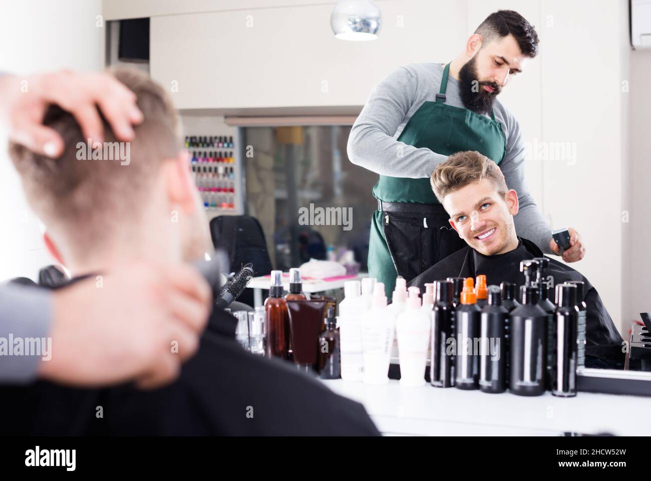 Young guy stylist creating haircut for joyous man client at