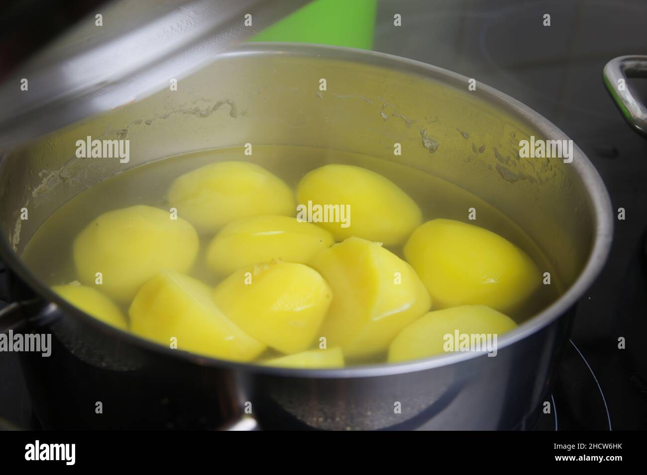 Closeup of pot on hotplate with raw potatos in steaming hot water and fork -  cooking time concept Stock Photo