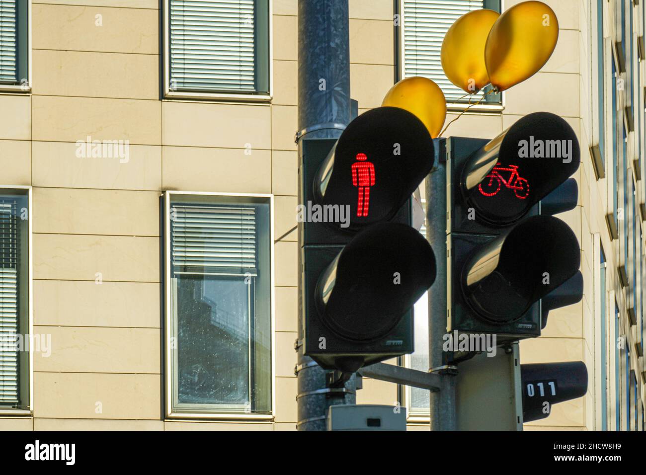 Three orange balloons hang from a traffic light above a pedestrian sign and bicycle sign set to red. Stock Photo